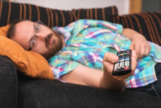 Man relaxing in sofa with remote control watching tv. Shallow dof focus on remote control.