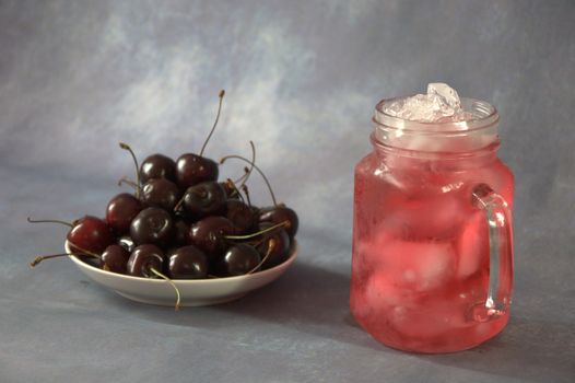 A plate with a bunch of ripe cherries and a glass of cherry juice with ice. Close-up.