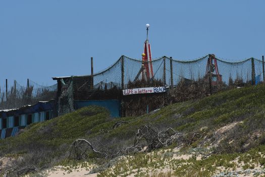 A large beach hide camp built with fishing nets and driftwood with plank banner stating "Life is better at beach", Mossel Bay, South Africa