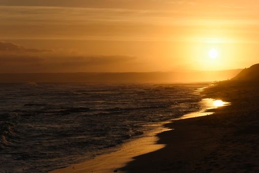 Sun setting over the bay shimmering on the wet sandy beach, Mossel Bay, South Africa