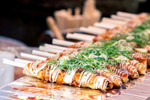Okonomiyaki on wooden sticks with soy sauce and mayonaise topped with green onion at Nishiki market, Kyoto, Japan