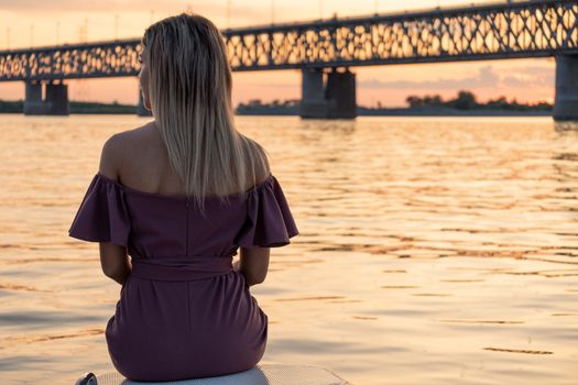 A young, beautiful and slender girl rides on the Amur river. Looking at the big bridge across the river