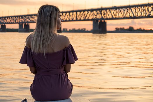 A young, beautiful and slender girl rides on the Amur river. Looking at the big bridge across the river