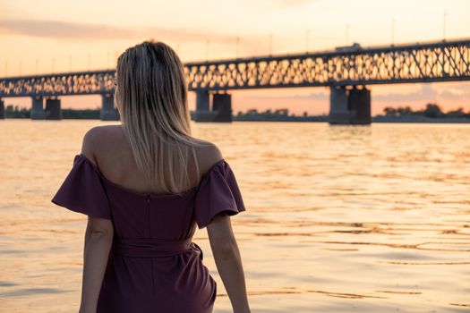 A young, beautiful and slender girl rides on the Amur river. Looking at the big bridge across the river