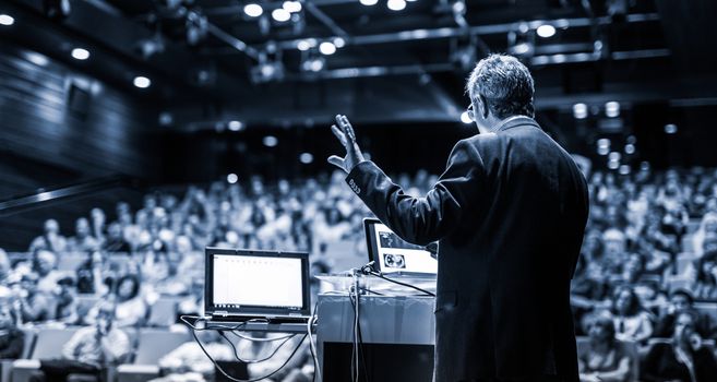 Speaker giving a talk on corporate business conference. Unrecognizable people in audience at conference hall. Business and Entrepreneurship event. Black and white, blue toned image.