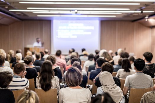 Speaker giving a talk in conference hall at business event. Audience at the conference hall. Business and Entrepreneurship concept. Focus on unrecognizable people in audience.