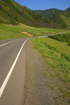 A good asphalt road running through a picturesque valley at the foot of a high hill. Altai, Siberia, Russia.