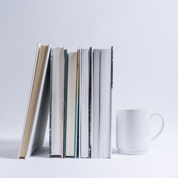 A white cup of coffee next to a row of books