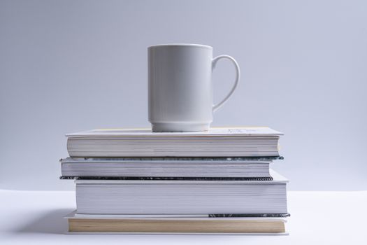 A white cup of coffee over a stack of books