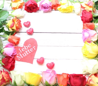 The picture shows a border with roses with a red heart with the german text dear mother.