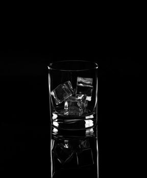 Glass with ice cubes a black background. Monochrome