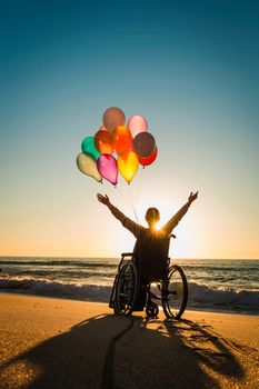 Handicapped woman on a wheelchair with colored balloons at the beach