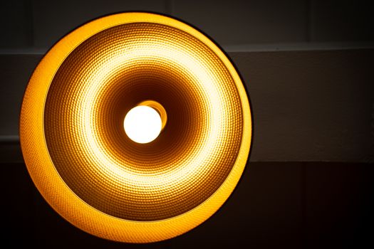 A Modern lamp hanging down from ceiling in the dark background. Minimalist chandelier with glowing warm light from bulb.