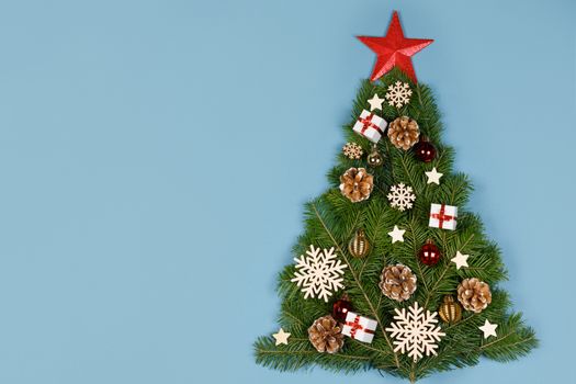 Christmas tree made of natural spruce branches deecor with red star on blue background, flat lay card with copy space