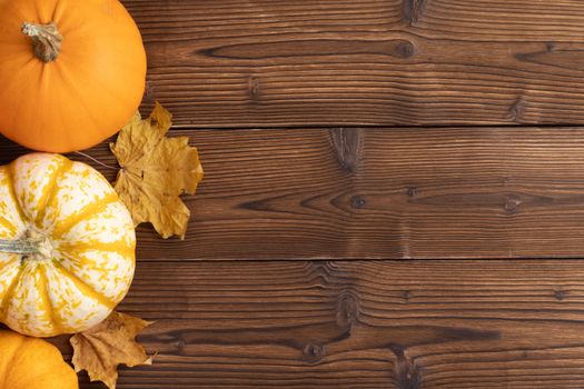 Striped yellow and orange pumpkins and dry maple autumn leaves on wooden background, top view, Halloween concept