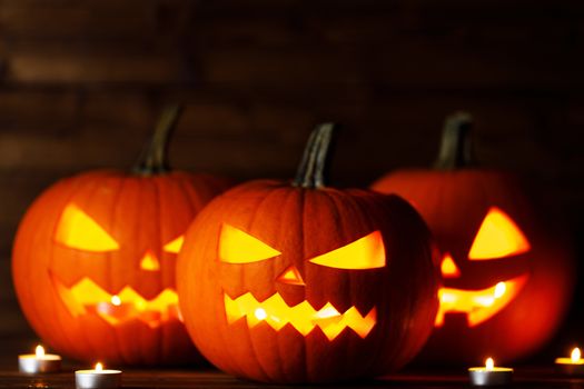 Three Halloween pumpkins head jack o lantern and candles on wooden table background