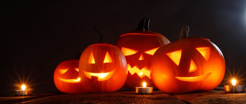 Many Halloween pumpkins head jack o lantern and candles on wooden table background