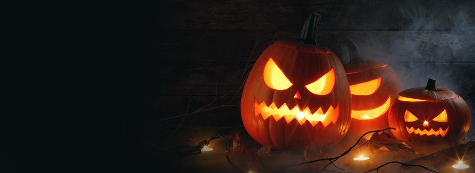 Halloween pumpkin heads jack o lantern and candles in fog on wooden background