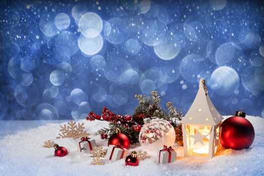Christmas holidays card with gifts , balls and glowing lantern in snow over blue bokeh lights background