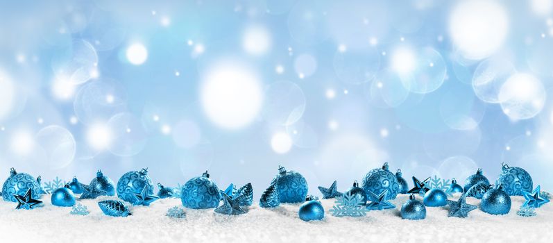 Christmas border with blue ornaments on snow on light bokeh background