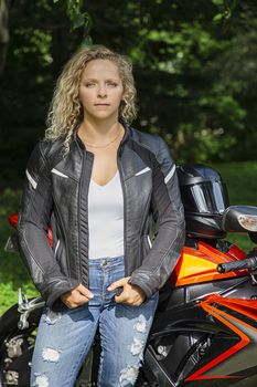 twenty something woman, wearing a black leather jacket, standing beside her sport motocycle