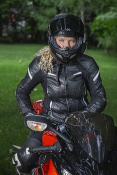 Twenty something woman, wearing full motocyclist outfit, sitting on a sport motocycle