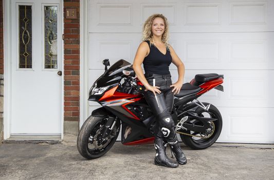 Happy twenty something woman, leaning on a sport motocycle, in front of garage door