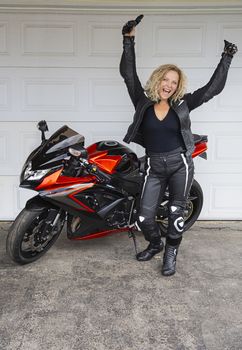 young blond woman with her arms in the air, standing in front of a sport motocycle