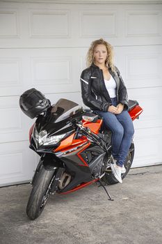 twenty something woman, sitting on a sport motocycle, standing in front of a garage door