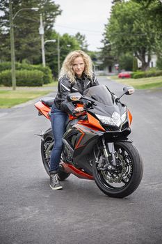 young blond woman, ready to ride a sport motocycle, in the middle of a suburb street