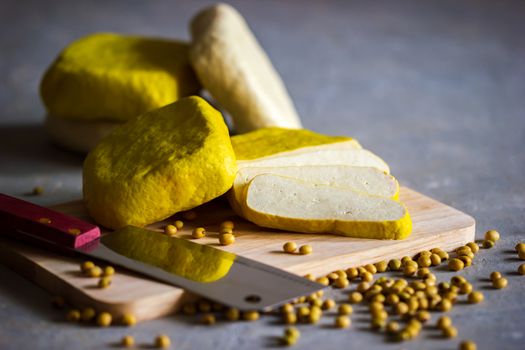 Fresh tofu is sliced on a wooden cutting board and soybean seeds scattered on the table. Healthy food concept.