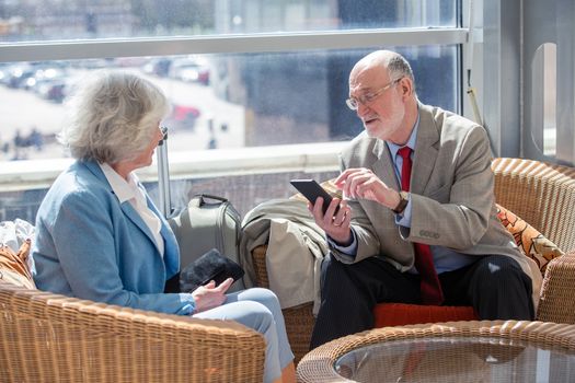 Senior couple of tourists waiting for their flight sitting with suitcase and talking