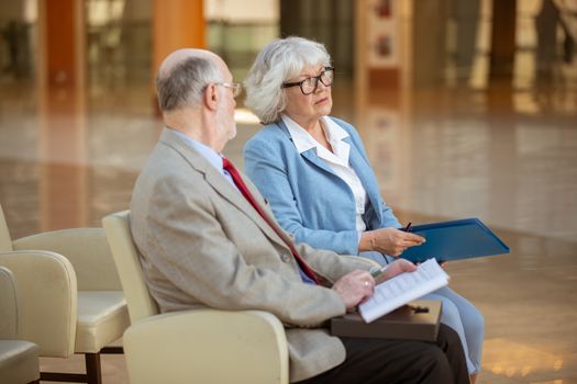 Senior people sitting in lobby and discuss documents