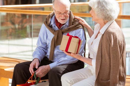 Senior woman giving a gift to her husband in shopping mall