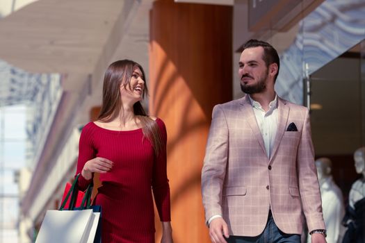 Happy beautiful young couple walking in mall holding shopping bags