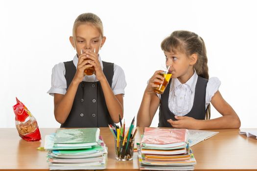 Two school friends drink juice at a table in a school class