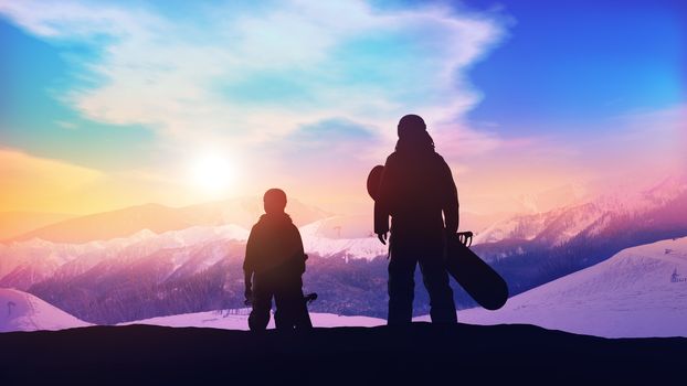 Father and son snowboarders looking at the setting sun in the snowy mountains.