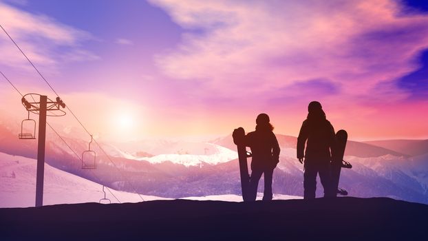 Two snowboarders looking at the setting sun in the snowy mountains.