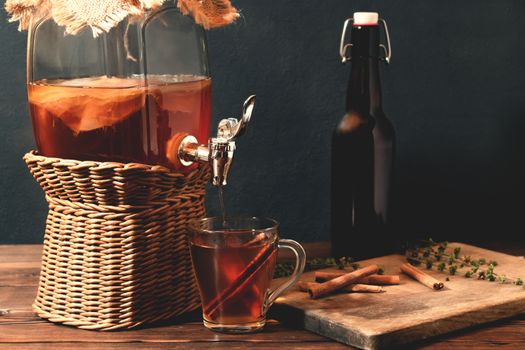 Fresh homemade Kombucha fermented tea drink in jar with faucet and in cup and bottle on black background.