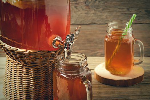 Fresh homemade Kombucha fermented tea drink in jar with faucet and in cans-mugs on wooden background.