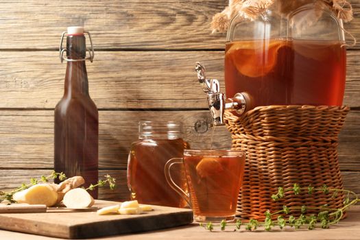 Fresh homemade Kombucha fermented tea drink in jar with faucet and in cans-mugs and cup on wooden background.