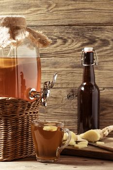 Fresh homemade Kombucha fermented tea drink in jar with faucet and in cup and bottle on wooden background, vertical image