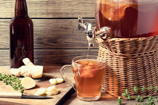 Fresh homemade Kombucha fermented tea drink in jar with faucet and in cup and bottle on wooden background.