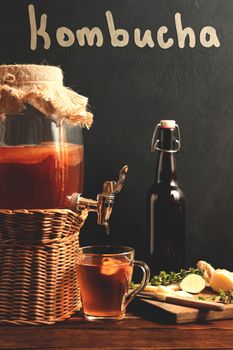 Fresh homemade Kombucha fermented tea drink in jar with faucet and in cup and bottle on black background, vertical image.