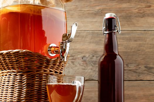 Fresh homemade Kombucha fermented tea drink in jar with faucet and in cup and bottle on wooden background.