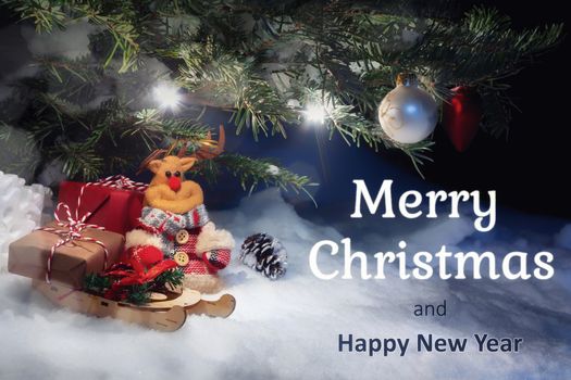 Christmas card - Christmas tree in the snow, gifts, toy deer and the inscription Merry Christmas and Happy New Year.