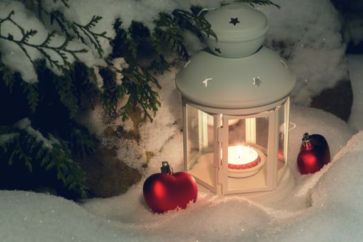 Lantern with a burning candle under a snow-covered Christmas tree in the courtyard of the house in the snowdrifts.