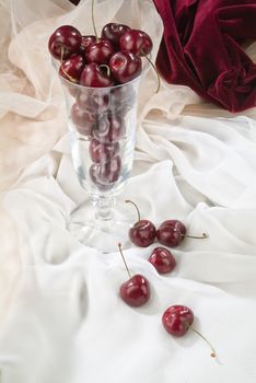Cherries and glass on a studio fabric background