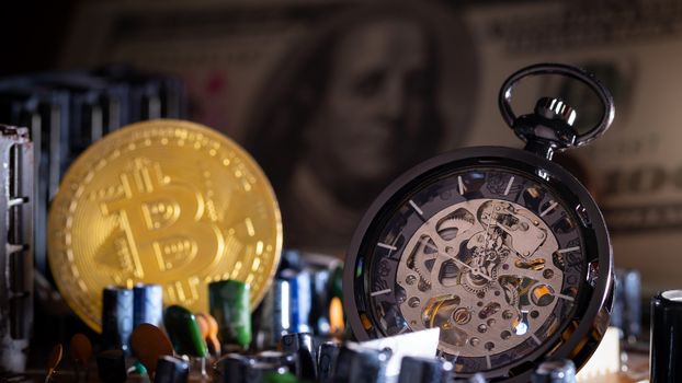 Pocket watch and gold bitcoin with dollar banknote on computer mainboard in darkness background.