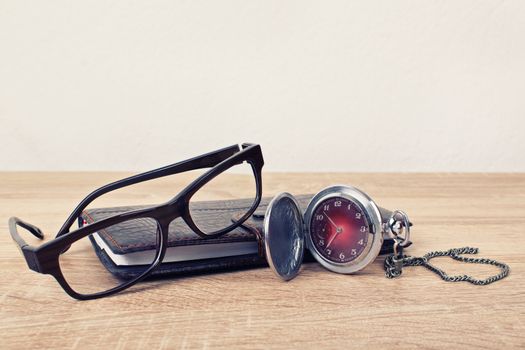 Close up shot of an antique pocket watch with glasses and a planner on a wooden background. Time for time travel.